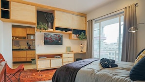 Ein Schlafzimmer mit Bett, Schreibtisch, Stuhl, Fenster und Blick auf die Stadt.