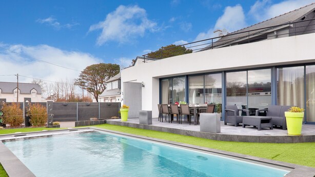 Une maison moderne dotée d’une piscine, d’un espace salon extérieur et d’une grande fenêtre donnant sur la cour.