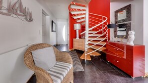 Un intérieur moderne avec un canapé en osier, un escalier en colimaçon rouge et une porte blanche.