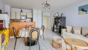Una cocina moderna con armarios blancos, una mesa de comedor con sillas, una estantería y un sofá en la sala de estar.