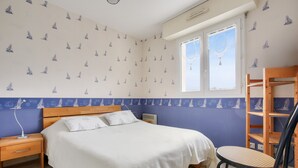 Un dormitorio con cama, mesita de noche, una silla y una ventana con cortinas.