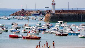 Un puerto con numerosos barcos amarrados, un faro y gente en la orilla.