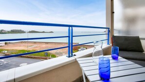 Un balcón con vista al mar, una mesa con dos vasos y una barandilla azul.