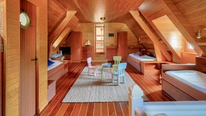 Ein gemütliches Schlafzimmer unter dem Dach mit Holzwänden und schrägen Decken, ausgestattet mit einem Bett, einem Schreibtisch und einem Stuhl.