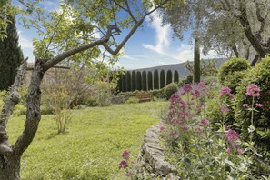 Stroll through a tranquil garden surrounded by lush plants and trees, with a serene stone wall and a comfortable bench.