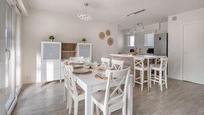 A modern kitchen with white cabinetry, a dining area with white chairs and a table set for four, and a large window providing natural light. - Flat for 5 at 600m from the beach (La Baule-Escoublac)