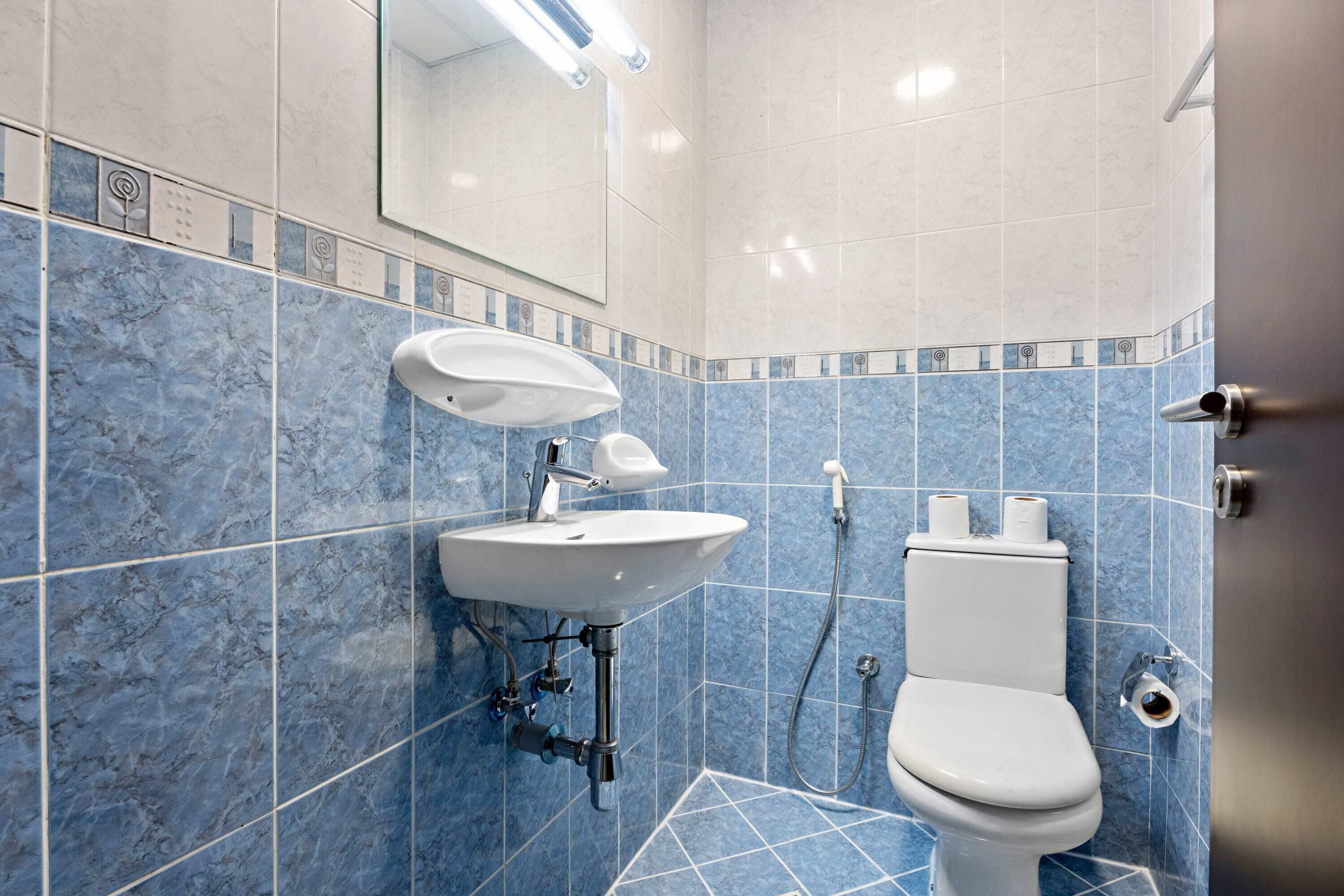 A bathroom with a sink, toilet, and blue-tiled walls.