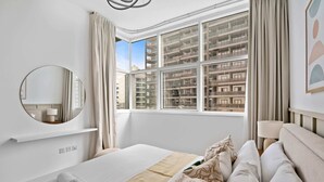 A modern hotel room with a large bed, a round mirror, a view of a high-rise building, and a window with curtains. - Silkhaus Uniestate Sports Tower - DSC (Dubai)