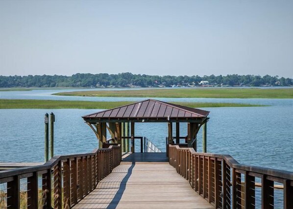 A wooden pier leading to a gazebo over water with a forested shoreline in the background.