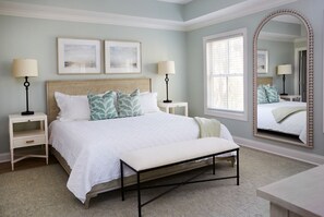 A bedroom with a large bed, two bedside tables, a bench, a mirror, and framed artwork on the wall.