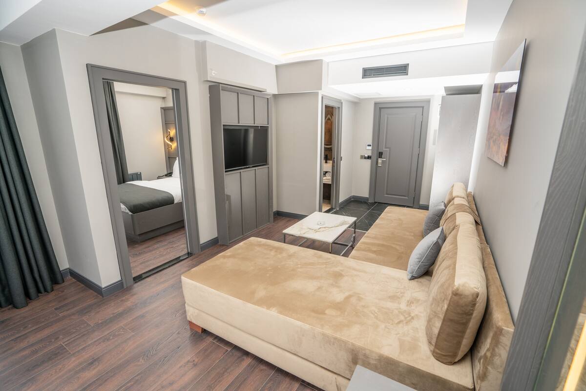 A modern hotel room with a large sofa, a TV, a small table, and a wardrobe.
