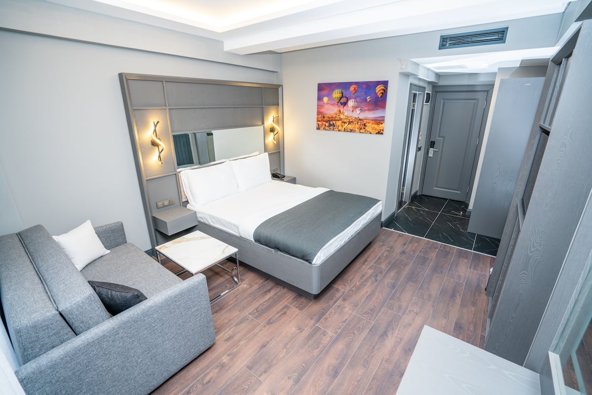 A modern hotel room with a bed, a sofa, a desk, and a painting on the wall.