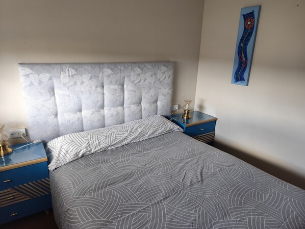 A neatly made bed with a patterned bedspread and pillows, flanked by two bedside tables with lamps and a power outlet.