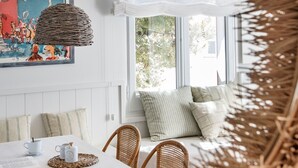 A dining area with a table, chairs, a hanging light fixture, a window with a view of greenery, and a wall-mounted painting. - Appartement 2 Chambres Pour 4 Personnes (Llançà)