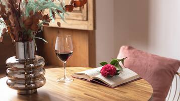Une table ronde en bois, sur laquelle se trouvent un livre, un verre de vin rouge et un vase rempli de fleurs séchées.