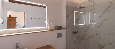 Un baño moderno con tocador de madera, un espejo grande, cabina de ducha de vidrio y paredes de mármol.