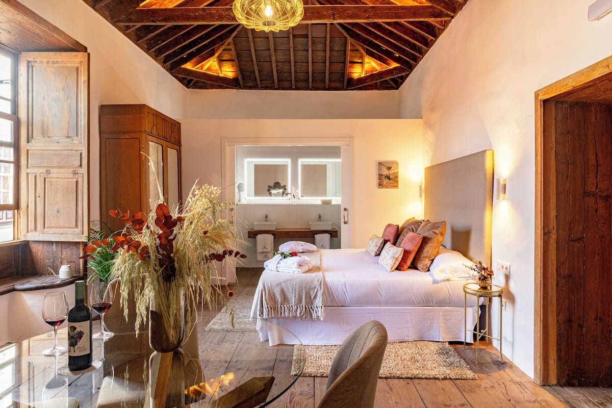 Um quarto aconchegante com teto de madeira, uma cama com almofadas, uma mesinha de cabeceira e uma janela com vista.