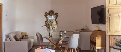 A cozy room with a glass-top dining table, a sofa, a wooden cabinet, and a mirror with a decorative frame.