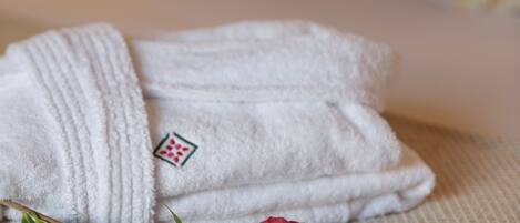 Una toalla blanca doblada con un logotipo, una flor rosa y hojas verdes sobre una superficie textil con textura.