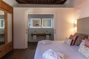 A bedroom with a wooden wardrobe, a bed with floral pillows, a bedside table, and a mirror with two lights. - Hotel Emblemático La Casa De La Camelia (San Cristóbal de La Laguna)