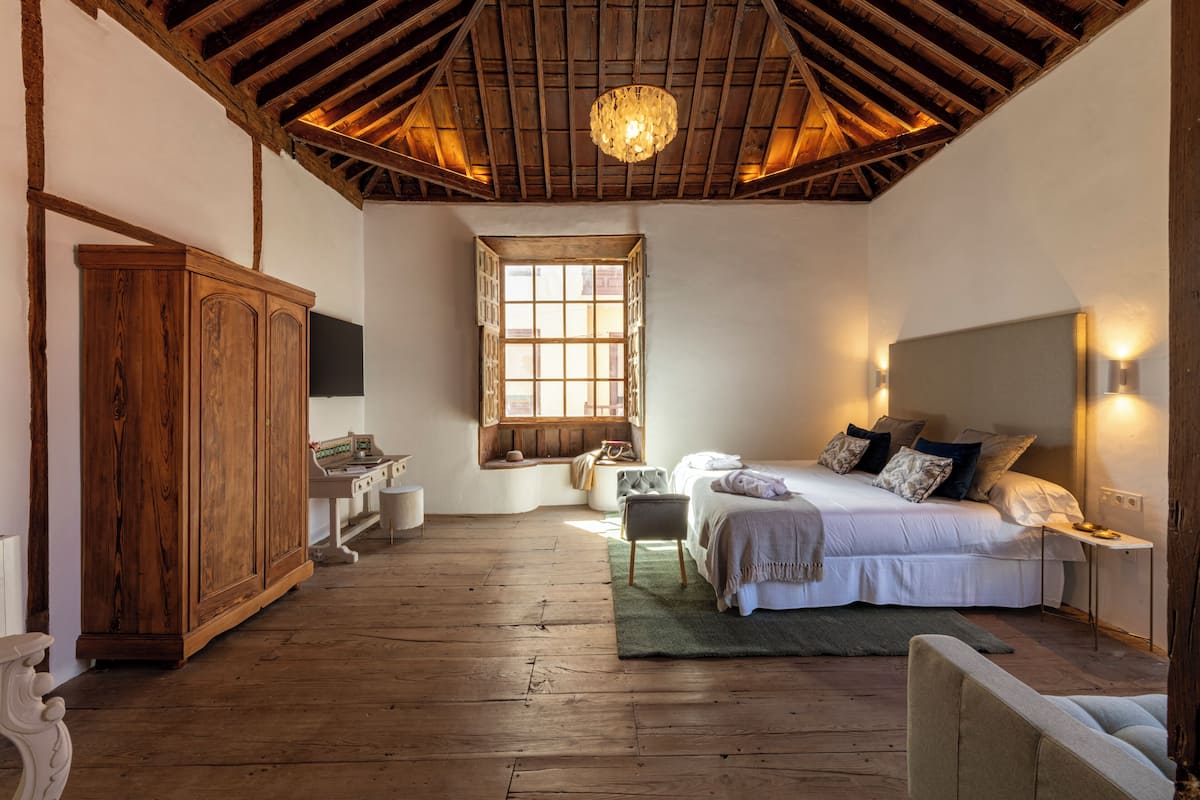 Quarto com teto de madeira, cama com almofadas, mesa de cabeceira e guarda-roupa de madeira.