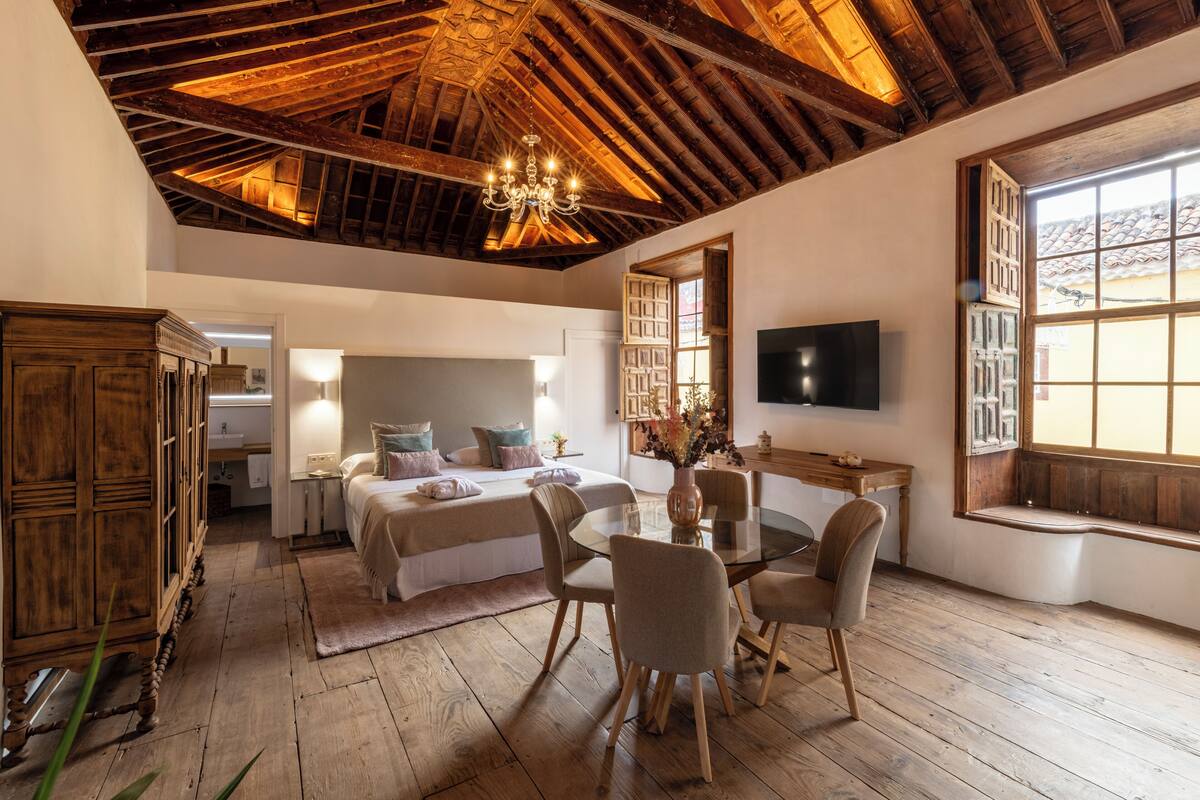 Um quarto espaçoso com uma cama grande, teto de madeira e televisão na parede.