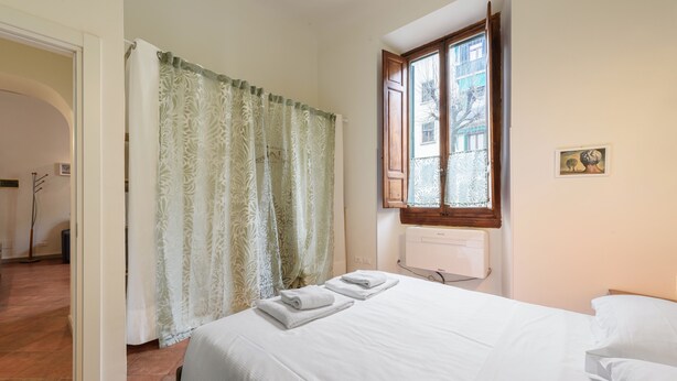 Un dormitorio con una cama, una ventana, un radiador y una puerta que da a otra habitación.