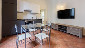 Una cocina moderna con una mesa de comedor y sillas, horno empotrado y un televisor montado en la pared.