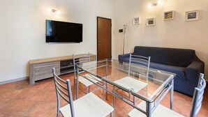 Una sala de estar moderna con una mesa de comedor de vidrio, un sofá, un televisor de pantalla plana y un mueble de madera.