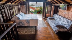 A cozy room with a bed, a sofa, and a view of a green hammock outside. - Cabanas Rosa Mistica (Imbituba)