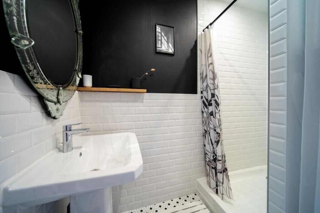 Een badkamer met een witte wastafel, een spiegel, een zwarte wand, een lijst met een afbeelding en een douchegordijn.