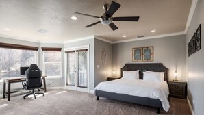 A bedroom with a large bed, a desk with a chair, a ceiling fan, and a view through the door. - Ping pong, Arcade, Private yard w/ Mountain view! (North Salt Lake)