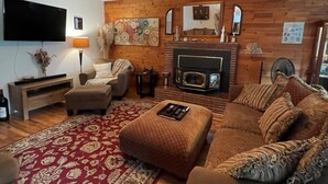 A cozy living room with a fireplace, wooden walls, a flat-screen TV, and a patterned rug. - Wild Orchards in the Camas Hills (Camas)