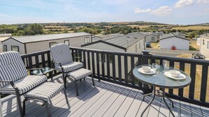 Terraza con mobiliario exterior y una mesa dispuesta para dos, con vista a una zona residencial con casas y campos abiertos.