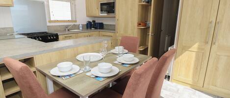 Cocina compacta con una isla central, armarios de madera y una zona de comedor con sillas rosadas.