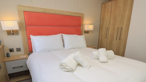 Habitación de hotel con una cama, dos mesitas de noche, un armario de madera y dos lámparas de pared.