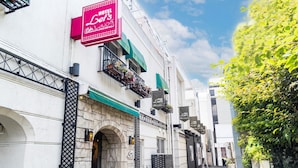 A narrow street with a building featuring a stone archway entrance, a red sign for "Hotel de la Borde," and balconies with flower boxes. - HOTEL Let's (Saitama)