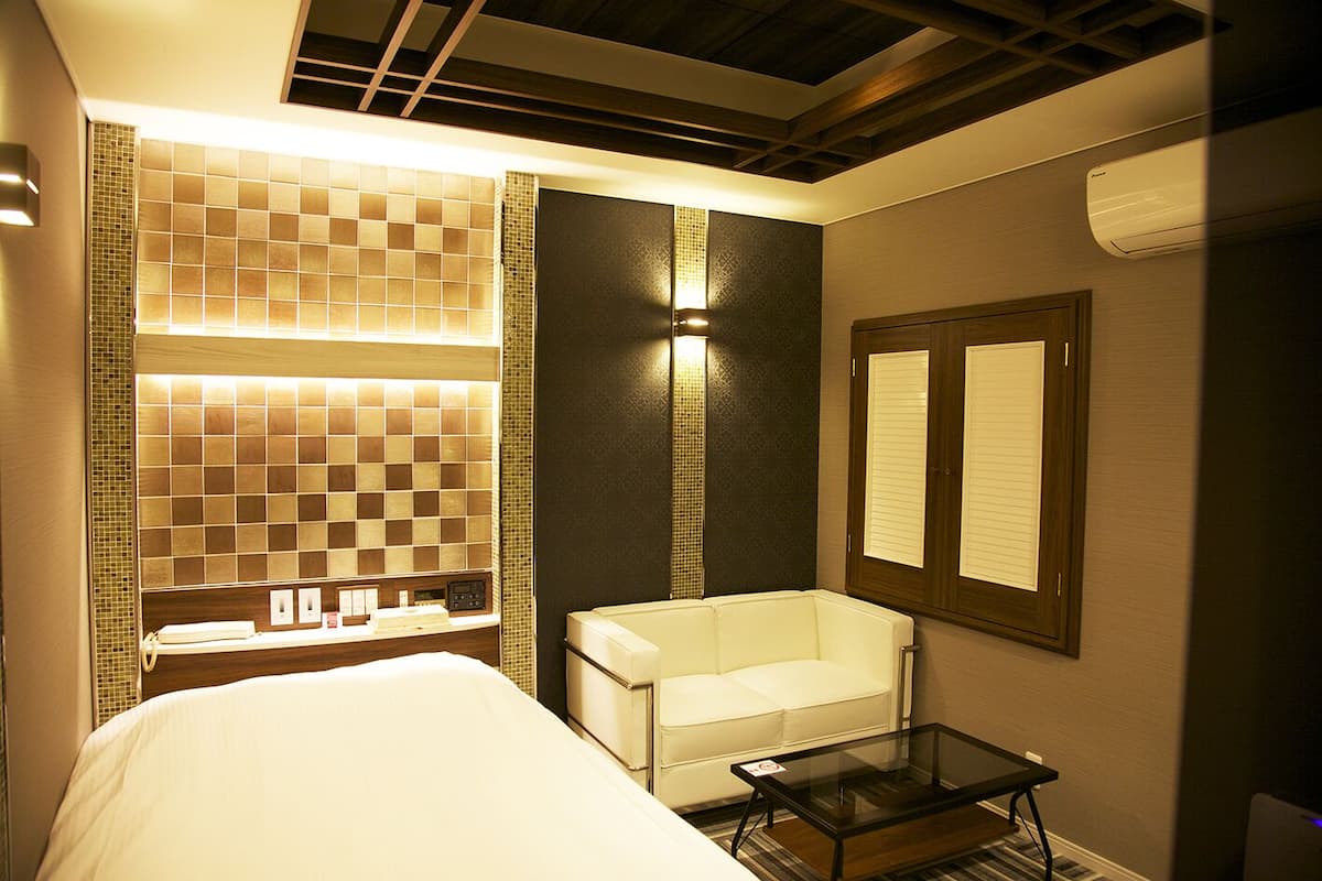 Quarto de hotel com cama, uma mesinha, uma cadeira, um espelho e uma parede com design de azulejos estampados.