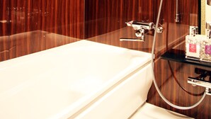 A modern bathroom with a wooden vanity, a white bathtub, and a shower with a handheld hose. - HOTEL Let's (Saitama)