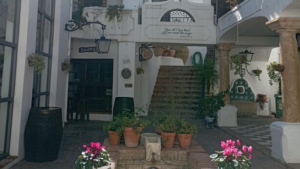 A courtyard with a central fountain, potted plants, and a building with a sign reading "Bodega". - Village house in Benahavis - right in the centre of the village (Benahavís)