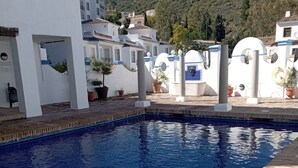 A swimming pool with a tiled deck, surrounded by white buildings with balconies and potted plants. - Village house in Benahavis - right in the centre of the village (Benahavís)