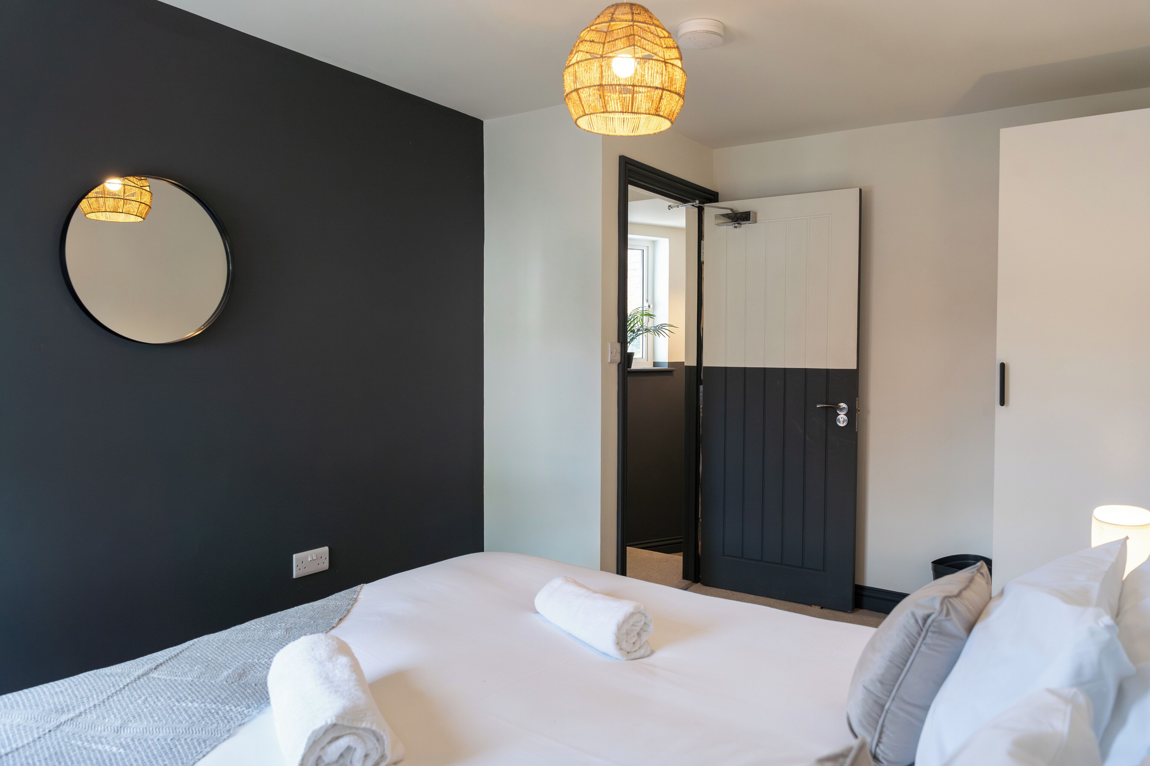A hotel room with a bed, a round mirror, a door, and a hanging light fixture.