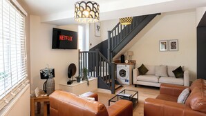 Una sala de estar con un sofá, una mesa de centro, un televisor, una lavadora y una escalera.