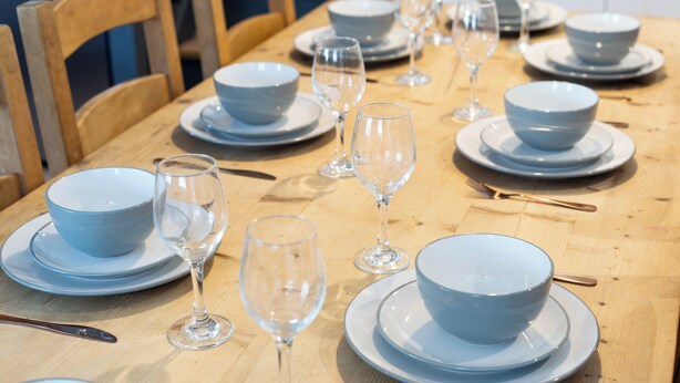 Una mesa de comedor dispuesta con cuencos, copas de vino y cubiertos.