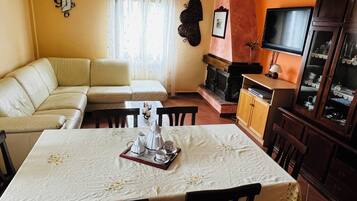 Ein Wohnzimmer mit einer Couch, einem Esstisch mit Stühlen, einem Kamin, einem Fernseher und einer Vitrine.