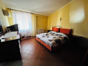 Een slaapkamer met een bed, een bureau, een stoel, een radiator en een klok aan de muur.