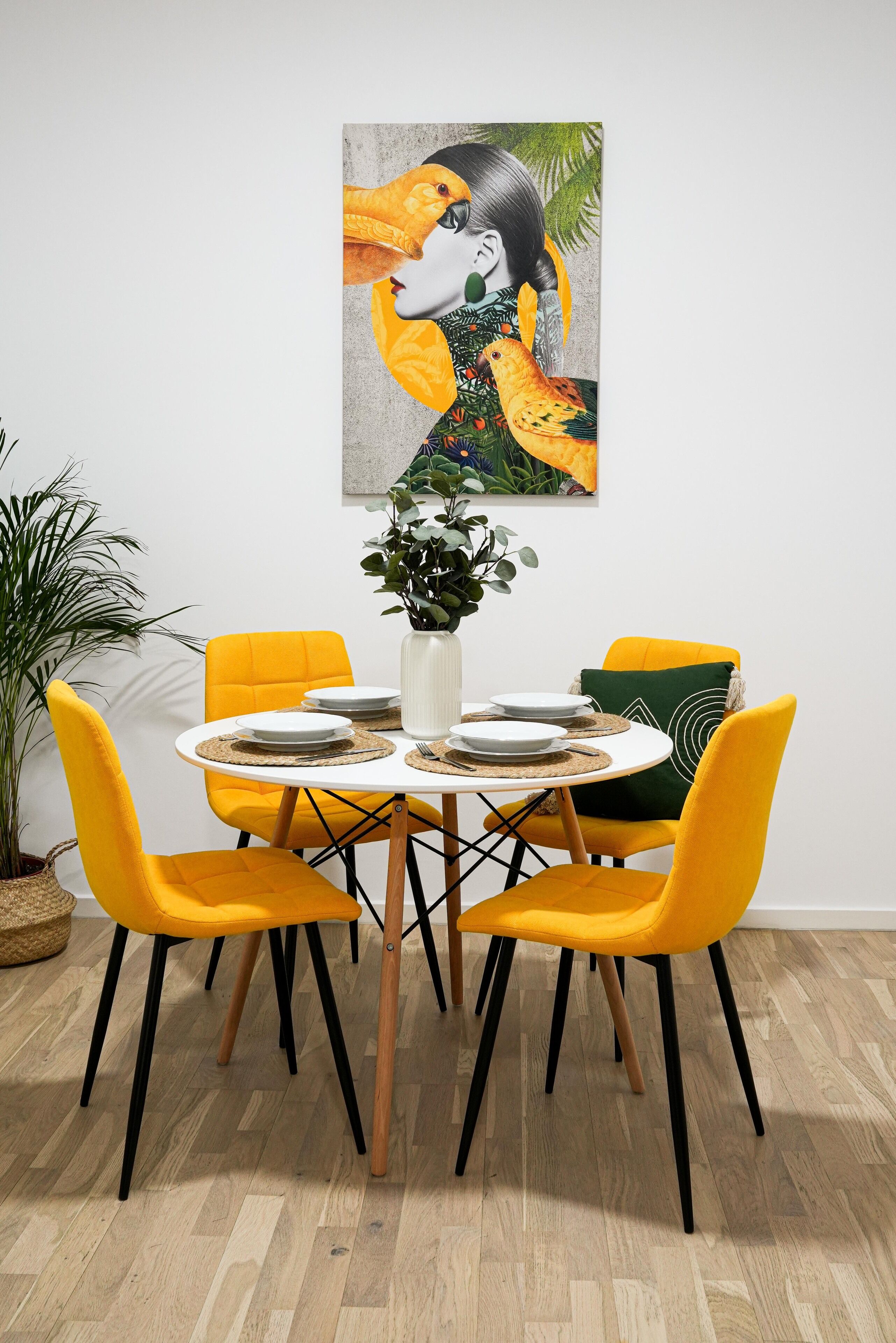 Un comedor con una mesa redonda, cuatro sillas amarillas y un cuadro en la pared.