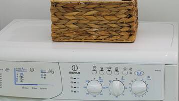 Una lavadora con una cesta de mimbre que contiene dos rollos de papel higiénico encima.