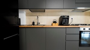 Una cocina moderna con gabinetes grises, encimera de madera, un hervidor, una cafetera y una estufa.