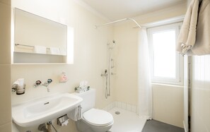 A bathroom with a sink, toilet, shower, and a window.